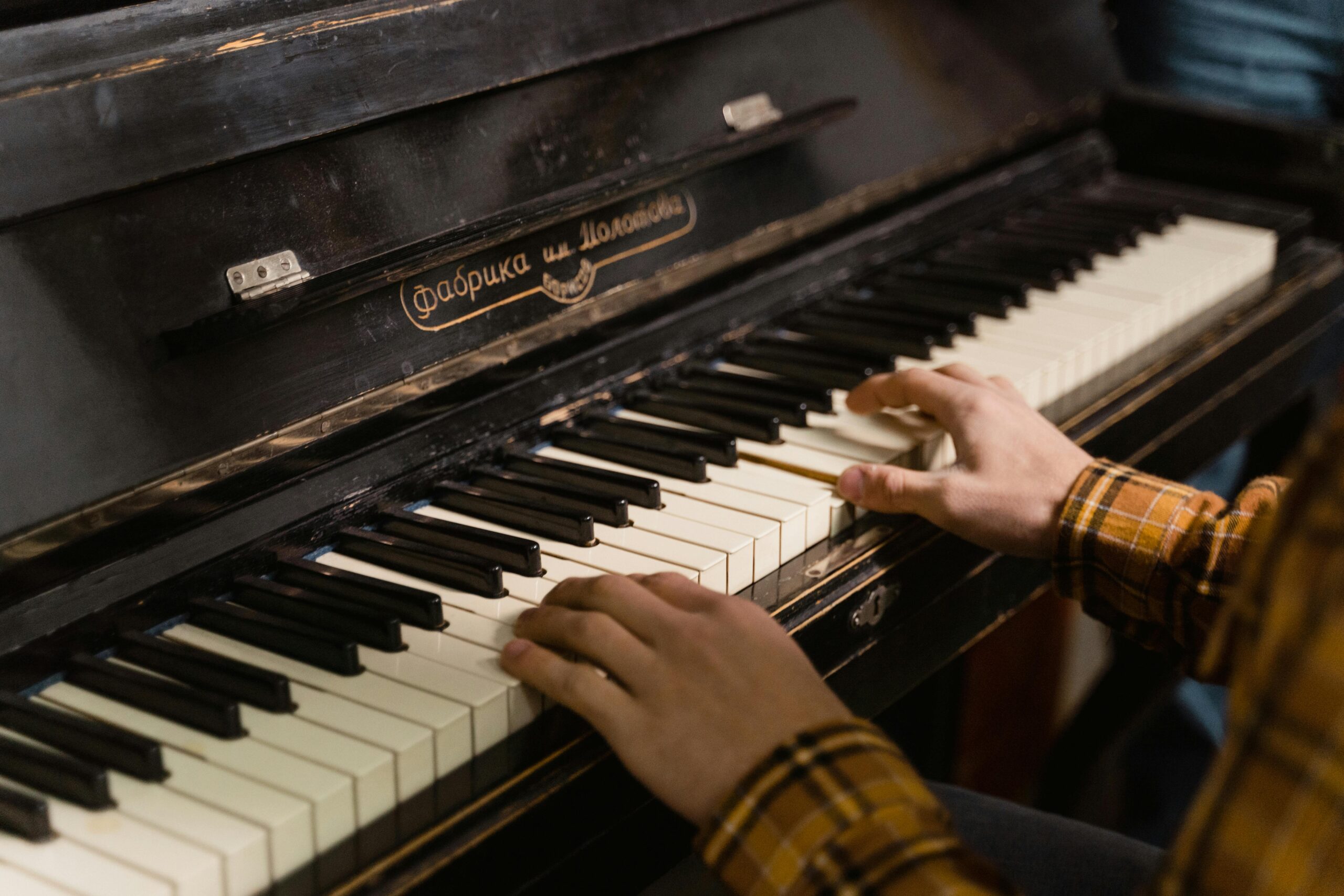 Close-up of hands playing a vintage piano with Russian brand label in a cozy indoor setting.
